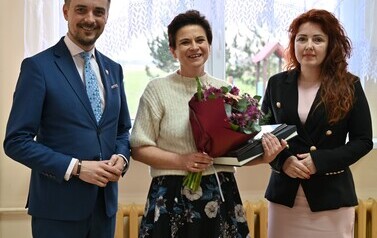 widzimy panią, pana oraz drugą panią trzymającą podarunek i bukiet kwiat&oacute;w w dłoniach 