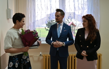 widzimy panią, pana oraz drugą panią trzymającą podarunek i bukiet kwiat&oacute;w w dłoniach 