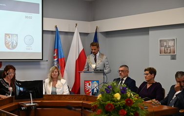 Siedzący radni pośrodku stoi przemawiajacy burmistrz