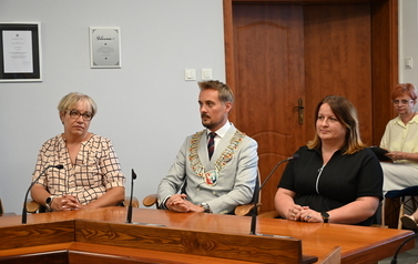 Siedzący radni oraz burmistrz przy stole klacjający w dłonie