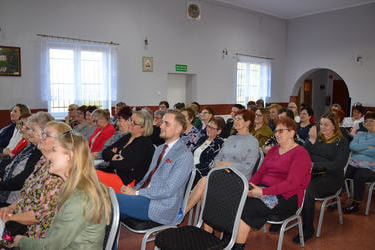 Na zdjęciu widać panie zebrane w Domu Kultury w Popowi Kościelnym. Kobiety siedzą na krzesłach, są uśmiechnięte i wpatrzone w scenę.