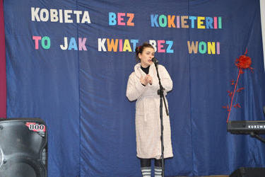 Na zdjęciu widać kobietę występującą na scenie. Ubrana jest w szlafrok i śpiewa