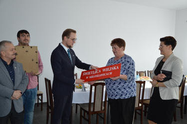 Na zdjęciu widać jak w&oacute;jt wręcza sołtysowi czerwoną tablicę z napisem Świetlica Wiejska. Pani sołtys jest bardzo wzruszona.