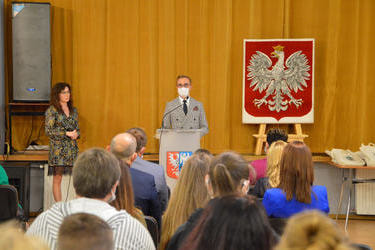 Na zdjęciu znajduje się W&oacute;jt Gminy Mieścisko - młody meżczyzna ubrany szarą marynarkę, białą koszulę. Wygłasza on przem&oacute;wienie przy m&oacute;wnicy, na tle godła Polski