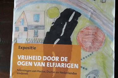 Na zdjęciu przedstawiony jets plakat wystawy pn. "Co znaczy dla ciebie wolność". Informacje umieszczone są w języku holenderskim. Tłem plakatu kest rysunek dziecka, kt&oacute;ry przedstawia domek, drogę, dziecko i drzewa.	