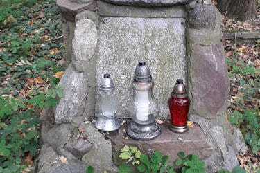 Na zdjęciu znajduje się stary kamienny gr&oacute;b, na nim stoją trzy znicze.