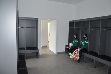 Na zdjęciu widać dw&oacute;ch chłopak&oacute;w w pomieszczeniu dla zawodnik&oacute;w. Jasne ścisny, szare nowoczesne specjalistyczne meble.