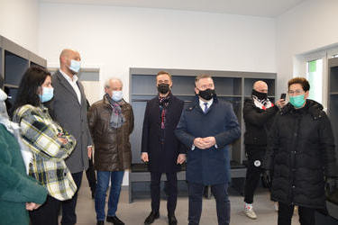 Na zdjęciu znajdują sie goście podziwiający wnętrze szatni. Jasne ściany, szare specjalistyczne meble. 