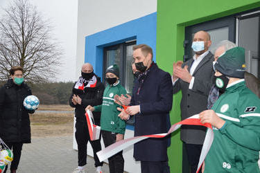 Na zdjęciu w&oacute;jt Gminy Mieścisko-młody mężczyzna w grantowym płaszczu przecina wstęgę. Ludzie wokoło klaszczą.