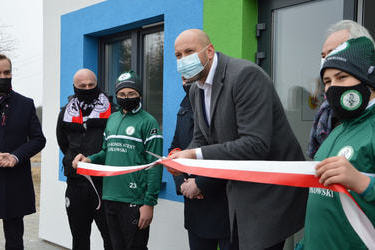 Na zdjęciu wysoki mężczyzna w szarym płaszczu- poseł Jakub Rutnicki przecina biało-czerwoną wstęgę.