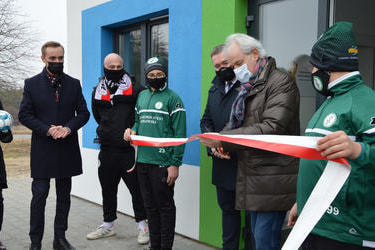 Na zdjęciu starszy siwy mężczyzna - senator Adam Szejnfeld w oliwkowej kurtce przecina biało-czerwoną wstęgę.