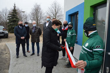 Na zdjęciu przewodnicząca Rady Gminy Mieścisko ubrana w czarną kurtkę przecina biało-czerwoną wstęgę trzymaną przez dw&oacute;ch chłopc&oacute;w w strojach piłkarskich.