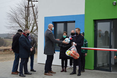 Na zdjęciu wysoki mężczyzna w szarym płaszczu- poseł Jakub Rutnicki wręcza w&oacute;jtowi piłkę.