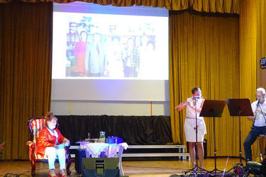 Na scenie kobieta i mężczyzna wykonują utw&oacute;r muzyczny na instrumentach. Jubilatka siedzi skupiona w wfotelu