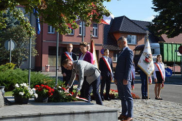 Na zdjęciu widać Pana W&oacute;jta składajacego wiązankę na pomniku. Obok stoi Pani Przewodnicząca Rady oraz Radny. W tle widać poczty sztandarowe