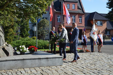 Na zdjęciu widać delegację podchodzącą do pomnika w celu złożenia wiązanki. W tle widać poczty sztandarowe
