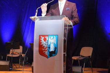 Na zdjęciu widać W&oacute;jta Gminy Mieścisko stojącego przy m&oacute;wnicy z herbem gminy. Ubrany jest w garnitur. 