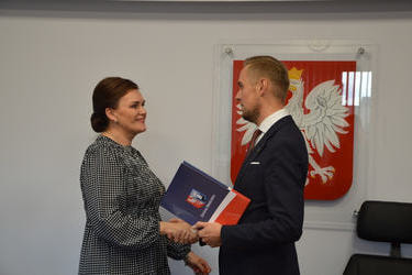 Na zdjęciu W&oacute;jt Gminy Mieścisko wręcza nagrodę nauczycielce w ciemnych, spiętych włosach. Uśmiechnięta kobieta ubrana jest w sukienkę w drobną, biało-czarną kratkę.