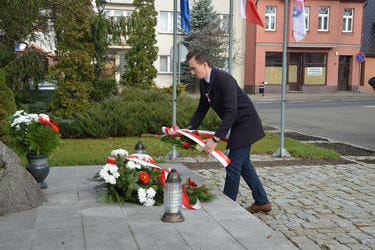 Zdjęcie przedstawia młodego mężczyznę składającego wiązankę na pomniku.