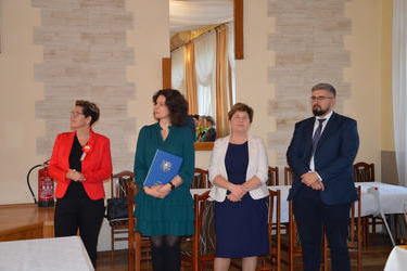 Na zdjęciu widać komisję oceniającą uczestnik&oacute;w. Od lewej strony kobieta w kr&oacute;tkich włosach, w czerwonym zakeicie. Obok kobieta w ciemnych, kręconych włosach w zielonej sukience. Następnie pani w granatowej sukience i jasnym żakeicie. I pan w okularach.