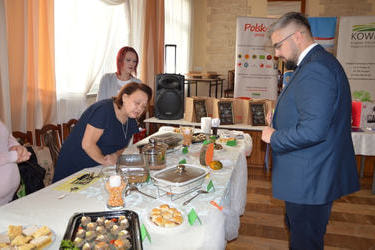 Na zdjęciu widać cżłonka komisji wysokiego mężczyznę, oceniającego potrawy przy stoisku Jaroszewa Pierwszego.