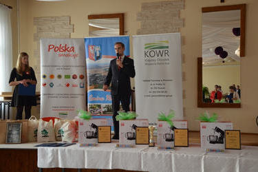 Na zdjęciu widać przemawiającego w&oacute;jta. Stoi na scenie. Przed nim wystawione są nagrody dla uczestnik&oacute;w VI Festiwalu Smak&oacute;w.