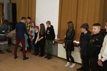 Na zdjęciu w&oacute;jt składa gratulacje dzieciom, kt&oacute;re występowały. Dzieci stoją przed sceną.
