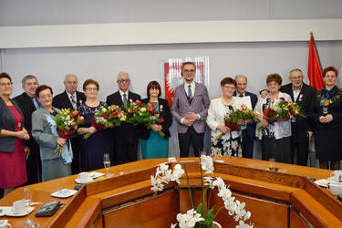 Zdjęcie przedstawia wszystkich jubilat&oacute;w wraz z przewodniczącą rady gminy, w&oacute;jtem oraz kierownikiem urzędu stanu cywilnego. Jubilatki w rękach trzymają bukiety kwiat&oacute;w. 