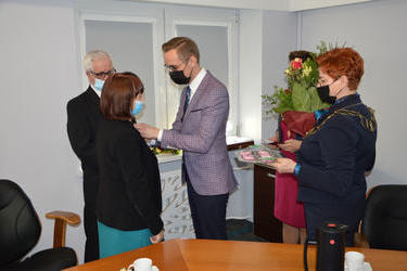 Na zdjęciu w&oacute;jt dekoruje jubilat&oacute;w orgerami. Kobieta ubrana w zieloną suknię i ciemny żakiet, mężczyzna w ciemnym garniturze. Obok stoi kierownik urzędu stanu cywilnego z bukietem kwiat&oacute;w.