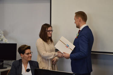 Na zdjęciu w&oacute;jt wręcza dokumenty i gratulacje młodej radnej. Jest to dziewczyna w ciemnych włosach, ma okulary i jasną sukienkę.