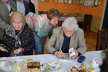 Na zdjęciu pisarz podpisuje swoje tomiki poezji zebranym gościom.