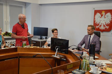 Jeden z gości z Francji stoi i trzyma w ręce kartkę. Reszta uczesnik&oacute;w siedzi.
