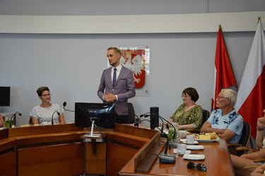 Na zdjęciu widać stojącxego W&oacute;jta i kilku gości. Na ścianie wisi godło. 