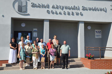 Grupowe zdjęcie na schodach przed budynkiem ZAZ-u. Goście z Francji i Holandii trzymają w rękach drobne upominki od zakładu. Wszyscy są uśmiechnięci.