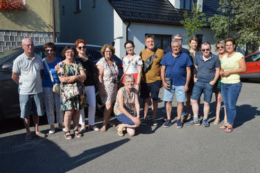 Zdjęcie grupowe gości z Francji i Holandii. Za nimi znajduje się samoch&oacute;d i budynki. Jedna z kobiet kuca. Wszyscy uśmiechnięci i kolorowo ubrani. 