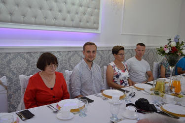 Goście siedzą przy stole i uśmiechają się do obiektywu.