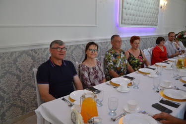 Goście siedzą przy stole i uśmiechają się do obiektywu.