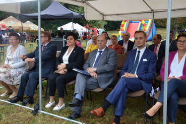 Zdjęcie przedstawia gości zaproszonych na dożynki. Siedzą na krzesłach w pierwszym rzędzie. Wszyscy elegancko ubrani.