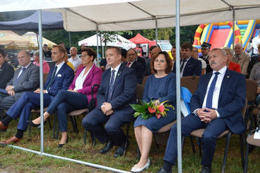 Zdjęcie przedstawia gości zaproszonych na dożynki. Siedzą na krzesłach w pierwszym rzędzie. Wszyscy elegancko ubrani.