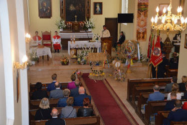 Zdjęci zrobione jest z ch&oacute;ru. Przedstawia ołtarz na kt&oacute;rym odprawiana jest msza.  Przed ołtarzem widać wieńce. W ławkach siedzą wierni.
