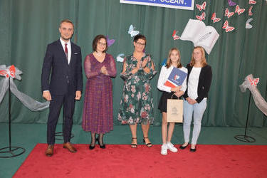 Zdjęcie przedstawia od lewej strony w&oacute;jta, panią dyrektor w okularach i śliwkowej sukni, następnie radna w kwiecistej sukience, obok nagrodzona dziewczynka w galowym stroju a obok niej mama.