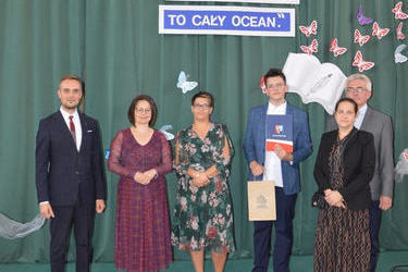 Zdjęcie przedstawia od lewej strony w&oacute;jta, panią dyrektor w okularach i śliwkowej sukni, następnie radna w kwiecistej sukience, obok stypendysta w eleganckim stroju, następnie jego rodzice