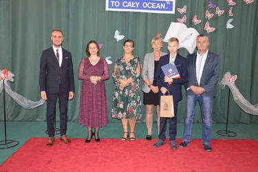 Zdjęcie przedstawia od lewej strony w&oacute;jta, panią dyrektor w okularach i śliwkowej sukni, następnie radna w kwiecistej sukience, obok mama stypendysty, następnie nagrodzony chłopak w eleganckim stroju i jego tata.