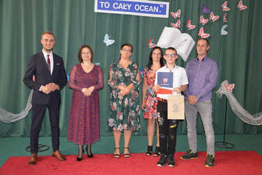 Zdjęcie przedstawia od lewej strony w&oacute;jta, panią dyrektor w okularach i śliwkowej sukni, następnie radna w kwiecistej sukience, obok stypendysta w galowym stroju, za nim stoją rodzice.