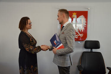 Zdjęcie przedstawia jak w&oacute;jt wręcza nagrodę pani dyrektor szkoły podstawowej w miescisku. Kobieta ma ciemne włosy za ucho, ubrana w ciemną sukienkę we wzory.