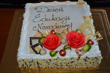 Zdjęcie przedstawia tort z napisem Dzień Edukacji narodowej. Ozdobiony jest czerwonymi kwiatami i dekoracjami z czekolady.