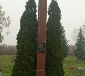Na zdjęciu widać duży drewniany krzyż, przed nim stoją znicze. 
