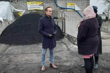 Na zdjęciu widać trzy osoby stojące koło hałdy węgla. Przodem stoi mężczyzna w płaszczu. Tyłem dwie kobiety.