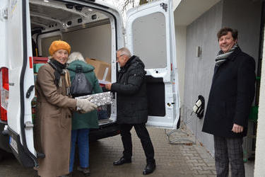 Zdjęcie przedstawia starszych ludzi wypakowujących prezenty z busa. 