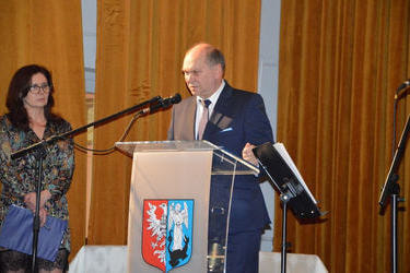Zdjecie przedstawia przemowę starszego mężczyzny. Jest on elegancko ubrany.